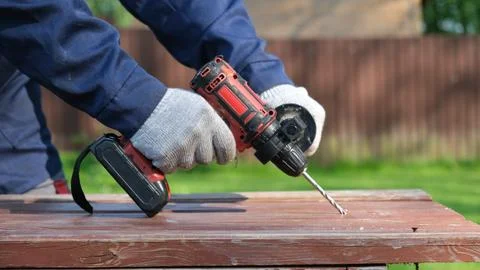 A close-up of a worker in a blue jacket and protective gloves drilling a ho.. Stock Photos