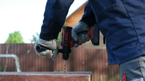 A close-up of a worker in a blue jacket and protective gloves drilling a ho.. Stock Photos
