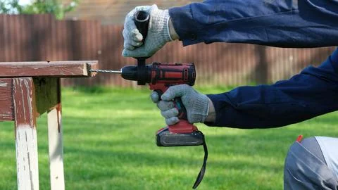A close-up of a worker in a blue jacket and protective gloves drilling a ho.. Stock Photos