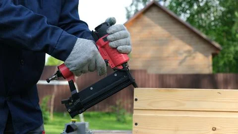 Close-up of worker in blue uniform and safety gloves using a red pneumatic na Stock Photos