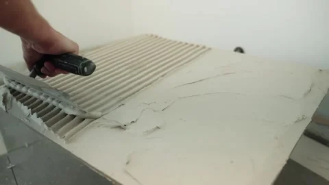 Close-up of a worker combing fresh tile adhesive with a notched trowel, forming Stock Footage 346260105