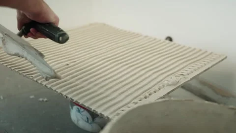 Close-up of a worker combing tile adhesive into uniform ridges on the back of a Stock Footage 345833885