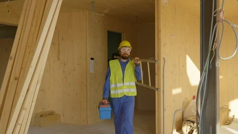 CLOSE UP: Worker coming to work carries his toolbox and ladder across the room. Stock Footage 124930378