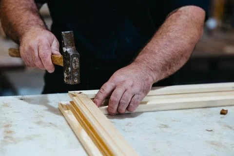 Close-up of worker hammering window frame corner during wood assembly Stock Photos