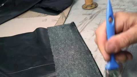 Close-Up Worker Hand Applying Glue to Leather Jacket Piece with Brush Stock Footage 322057743