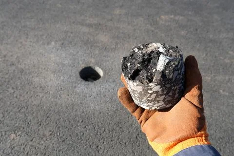 Close-up of a worker hand in an orange protective glove holding an asphalt co Stockfoto's