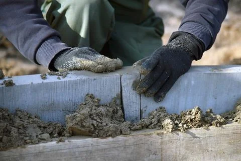 Close-up of a worker leveling installed concrete curbs in cement. Stock Photos