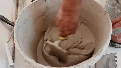 Close-up of a worker mixing tile adhesive in a bucket with a trowel during an Stock Footage 345068060