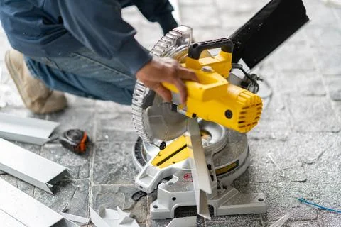 Close-up of a worker operating a yellow power miter saw to cut an aluminium.. Stock Photos
