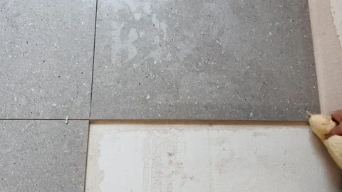 Close-up of a worker positioning a large gray floor tile beside spacers during Stock Footage 345068078