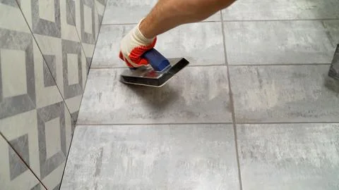 Close up of worker in protective glove applying grout to grey ceramic floor.. Stock Photos