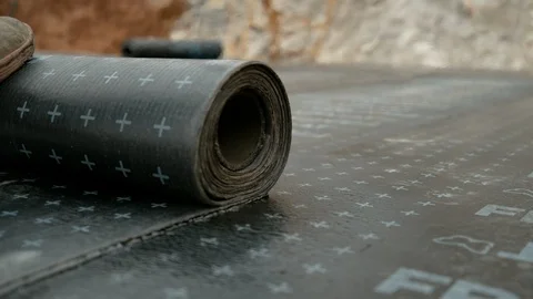 CLOSE UP: Worker rolls out tar paper with his foot while waterproofing a house. Stock Footage 120062962