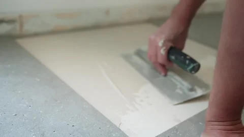 Close-up of a worker smoothing fresh tile adhesive across a floor substrate Stock Footage 345833916