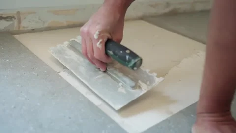 Close-up of a worker smoothing fresh tile adhesive across the floor substrate Stock Footage 346021643