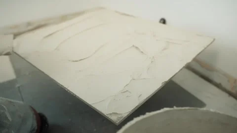 Close-up of a worker spreading adhesive across the back of a large floor tile Stock Footage 345833873