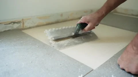 Close-up of a worker spreading fresh tile adhesive over an exposed substrate Stock Footage 345833898
