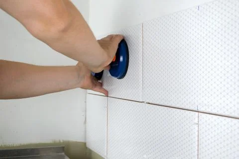 Close-up of worker tiler hands installing white ceramic tiles on walls of fut Stock Photos