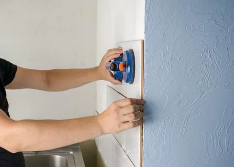 Close-up of worker tiler hands installing white ceramic tiles on walls of fut Stock Photos