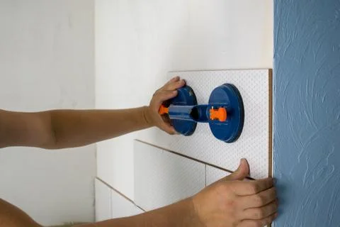 Close-up of worker tiler hands installing white ceramic tiles on walls of fut Stock Photos