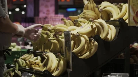 Close-up worker in uniform and gloves in supermarket sorting through bananas in Stock Footage 136634062