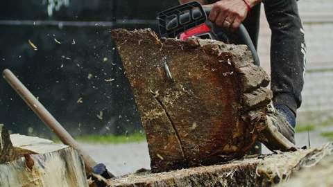 Close-up of a worker using a chainsaw to cut a thick log, with wood chips and Vídeos de archivo 304357126