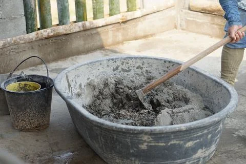 Close up worker using a hoe to mix cement powder, sand, stones in basin for mixi Stock Photos