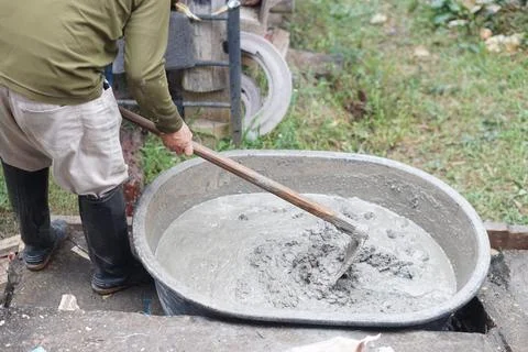 Close up worker using a hoe to mix cement powder, sand, stones in basin for mixi Foto stock