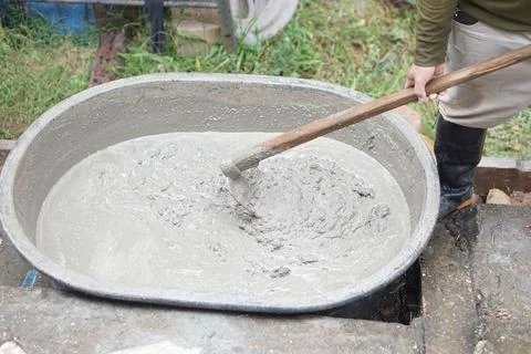 Close up worker using a hoe to mix cement powder, sand, stones in basin for mixi Stock Photos
