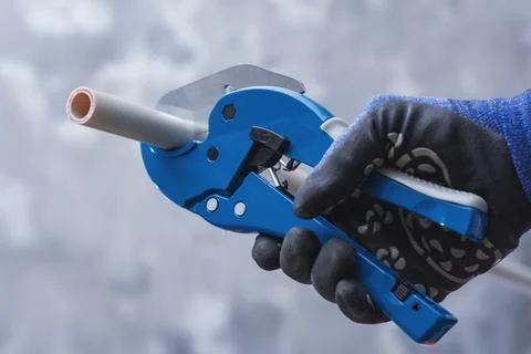 Close up of worker using pipe cutter to cut plastic PVC pipe during plumbing  Stock Photos