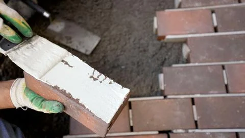 Close up of a worker's hands applying mortar to a brick for paving or const.. Stock Photos