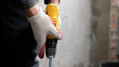 Close up of worker's hands in protective gloves holding yellow cordless pow.. Stock Photos