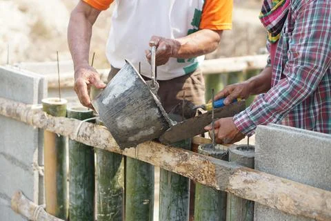 Close up workers help each other to pour cement into bamboo molding for building Stock Photos