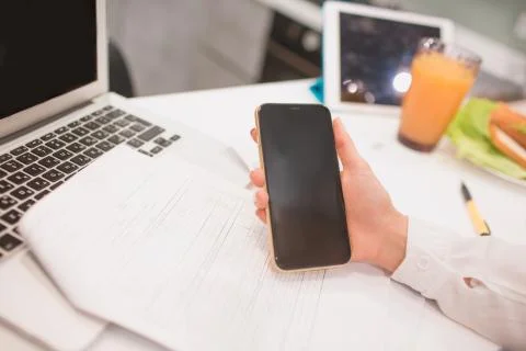 Close-up workplace in the kitchen. Smartphone in hand A woman works from home Stock Photos