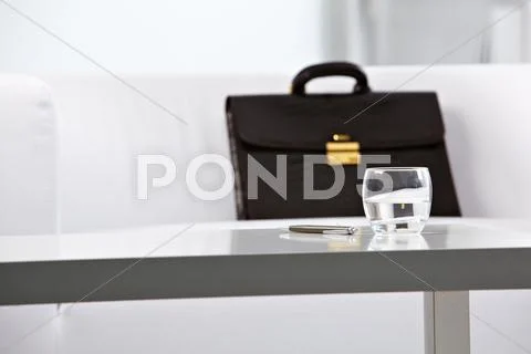 Close-up of workplace in office with glass of water, pen and briefcase on backgr Stock Photos