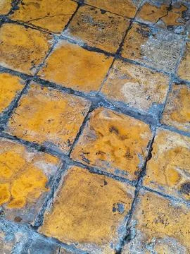 Close up of worn yellow ceramic tiles with dark grout and chipped edges, show Stock Photos