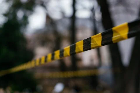 A close-up of a yellow and black caution tape stretched across an outdoor scene Stock Photos