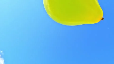 Close-up yellow balloon approaches camera on bright blue sky Stock Footage 325323468
