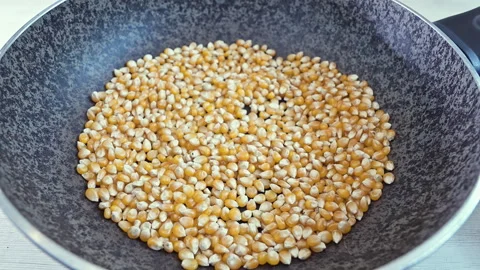 Close-up of yellow corn kernels falling into a frying pan for roasting Stock Footage 339078735