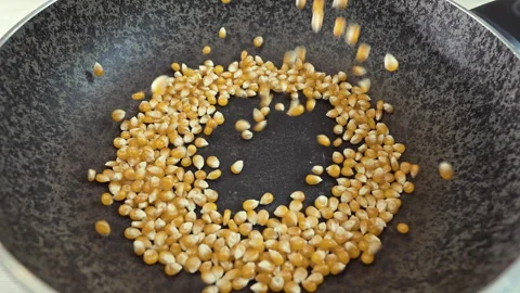Close-up of yellow corn kernels falling into a frying pan for roasting Stock Footage 339079272
