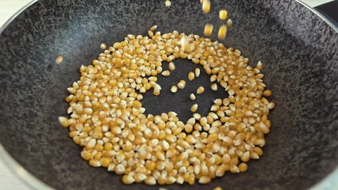 Close-up of yellow corn kernels falling into a frying pan for roasting Stock Footage 341440802