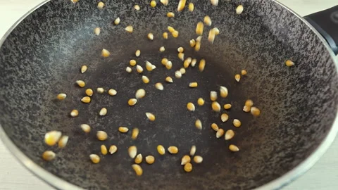 Close-up of yellow corn kernels falling into a frying pan for roasting Vídeo Stock 344990712