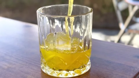 Close-Up of Yellow Drink Being Poured into Glass with Ice - Slow Motion Beverage Stock Footage 312694358