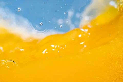Close-up of yellow liquid splash with bubbles and blue background Stock Photos