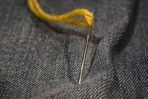 Close up, yellow needle and thread on jeans cloth Stock Photos