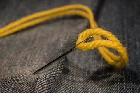 Close up, yellow needle and thread on jeans cloth Stock Photos