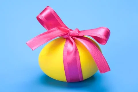 Close-up of yellow painted easter egg tied by red ribbon over blue background 스톡 사진