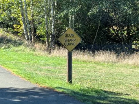 A close-up of a yellow “Slow Sharp Curve” road sign on a wooden post 库存照片