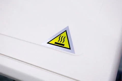 Close up of a yellow triangular hot surface warning sticker on the white me.. Stock Photos