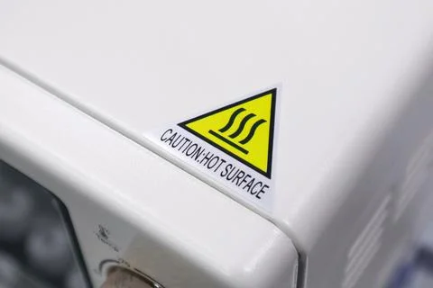 Close up of a yellow triangular hot surface warning sticker with caution te.. Stock Photos
