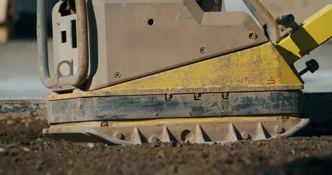 Close up of yellow vibratory plate compactor leveling soil at construction site Stockbeeldmateriaal 329564068